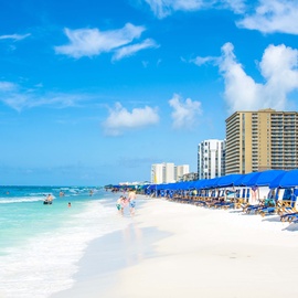 Just steps to the beautiful white sand beach with turquoise waters and comfortable beach chair rentals, backed by modern resort buildings under brilliant blue skies.