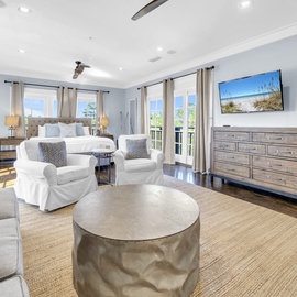 Your spacious master bedroom blends comfort with coastal elegance, featuring plush seating, a wall-mounted TV, and bright windows inviting natural light.