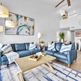 Sink into plush blue sofas in your airy living space, where coastal artwork and warm lighting create perfect moments for relaxation.