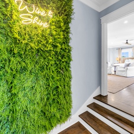Step into your stylish haven where a stunning living moss wall greets you with warm 'Wine & Shine' neon vibes.