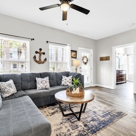 Relax in your spacious living room with plush sectional seating, coastal decor, and gentle ceiling fan breeze.