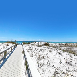 A wooden boardwalk leads through pristine white sand dunes to crystal-clear turquoise waters under brilliant blue skies.