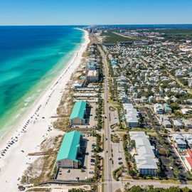 Stunning aerial view showcasing pristine white sand beaches meeting turquoise Gulf waters, with nearby coastal neighborhoods and convenient beachfront access.