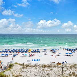 Pristine white sand beach stretching along emerald Gulf waters with colorful umbrellas and beach activities nearby.