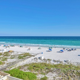 Pristine white sand beach stretches endlessly along crystal-clear turquoise waters under brilliant blue skies.