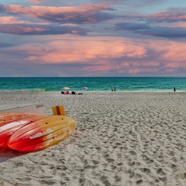 Stunning beachfront location with soft sand, clear waters, and colorful kayaks ready for adventure under dramatic sunset skies.