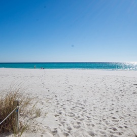 Just steps away from pristine white sand beach stretching along turquoise waters under brilliant blue skies, creating an idyllic coastal paradise.