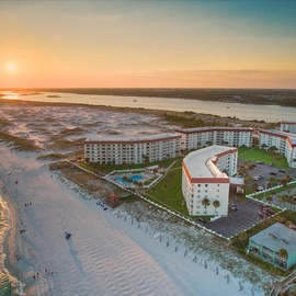 Beachfront resort buildings positioned along pristine white sand with the Gulf waters stretching to the horizon during golden hour.