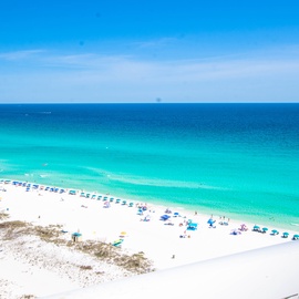 Pristine white sand beach with crystal-clear turquoise waters and colorful umbrellas dotting the shoreline.