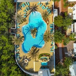 Stunning aerial view showcases the resort's expansive pool complex with curved lagoon-style design, tropical palm trees, and extensive sun deck surrounded by lush landscaping.
