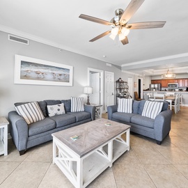 Relax in your bright, airy living space featuring comfortable seating and coastal decor, seamlessly connecting to your fully-equipped kitchen.