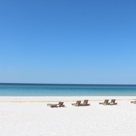 Pristine white sand beach with crystal-clear turquoise waters stretching to the horizon under brilliant blue skies.