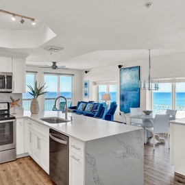 Your fully equipped kitchen flows seamlessly into the living space, where stunning ocean views through floor-to-ceiling windows create the perfect backdrop for cooking and relaxing.