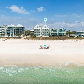 Beachfront vacation rental buildings line pristine white sand beach with crystal clear turquoise waters and gentle waves.