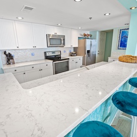 Your spacious kitchen features white quartz counters, stainless appliances, and cheerful turquoise accents that create the perfect backdrop for vacation meal prep.
