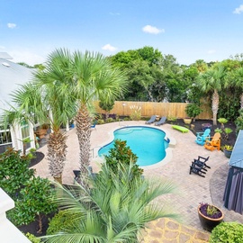 Aerial view of tropical vacation home featuring sparkling pool surrounded by lush palm trees and modern outdoor living spaces in a private setting.