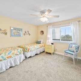 Unwind in your cheerful twin bedroom with soft coastal colors, comfortable seating nook, and gentle ceiling fan breeze.
