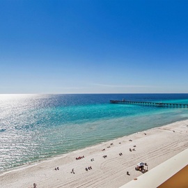 Stunning white sand beach stretches along crystal-clear turquoise waters with a scenic pier extending into the Gulf.