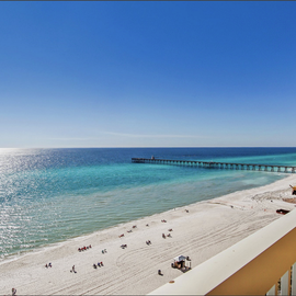 Stunning beachfront view with pristine white sand, emerald waters, and fishing pier stretching into the Gulf.