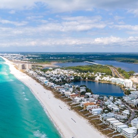 Aerial view capturing the stunning coastal neighborhood nestled between turquoise Gulf waters and a serene inland lake, showcasing the property's idyllic beachfront location.