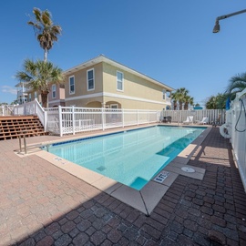 Coastal vacation rental community featuring swimming pool surrounded by tropical palms and colorful beach houses.