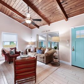 Relax beneath stunning vaulted wood ceilings in your charming living room, where coastal colors and cozy furnishings create the perfect beach retreat atmosphere.