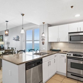 Your modern kitchen flows seamlessly into the dining and living areas, featuring granite countertops and ocean views through floor-to-ceiling windows.
