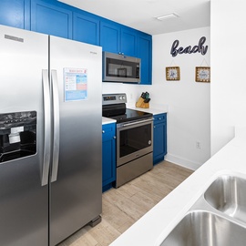 Your bright, beach-themed kitchen features vibrant blue cabinets and stainless steel appliances, creating a cheerful coastal atmosphere for your vacation cooking.