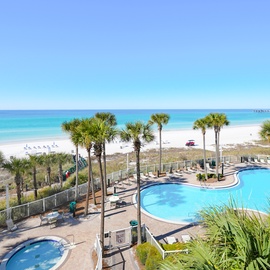 Beachfront resort featuring pools, palm trees, and pristine white sand beaches with turquoise waters stretching to the horizon.