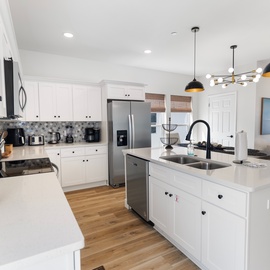 Your gourmet kitchen features pristine white cabinetry, stylish pendant lighting, and a spacious island—perfect for preparing meals and gathering with loved ones.