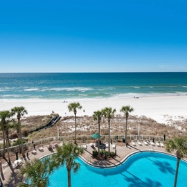 Stunning beachfront pool overlooks pristine white sand beach and crystal-clear Gulf waters under endless blue skies.