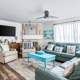 Sink into plush turquoise sofas in your spacious living room, where coastal charm meets modern comfort with a cozy fireplace and entertainment center.
