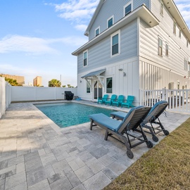 Modern coastal home featuring a private pool surrounded by stylish paver patio and tropical landscaping.