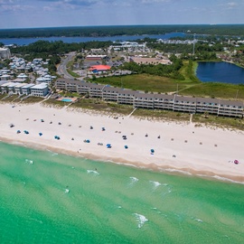 Stunning beachfront property surrounded by pristine white sand beach and emerald waters, with coastal town amenities nearby.