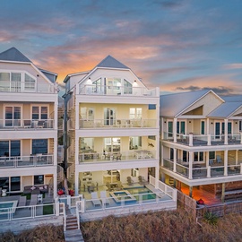 Modern beachfront vacation homes showcase stunning architecture and luxury amenities against a colorful sunset sky.