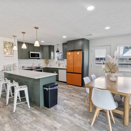 Step into your open-concept kitchen and dining area, where deep green cabinetry and modern brass fixtures create a sophisticated space for cooking and gathering. The island invites morning coffee while sunlight streams through bright windows.