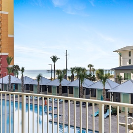 Beachfront resort view with pool, palm trees, and nearby accommodations under clear blue skies.