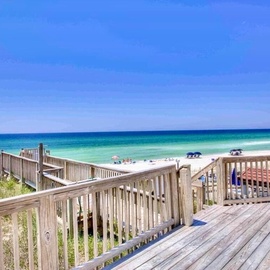 A wooden boardwalk deck frames pristine turquoise waters and white sand beaches stretching along the Gulf Coast. The property offers direct beach access steps from your vacation home.
