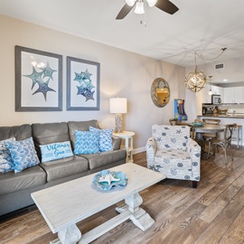 Relax in your coastal-themed living space with ocean artwork and comfortable seating flowing into a fully equipped kitchen.