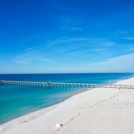 Pristine white sand beach stretching along turquoise waters with a fishing pier extending into the Gulf of Mexico near Panama City Beach.