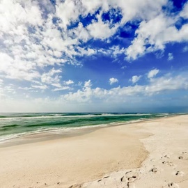 Pristine beach stretches endlessly with soft white sand and turquoise waves under dramatic blue skies.