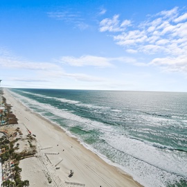 Stunning aerial view showcases the pristine coastline with wide sandy beaches, rolling surf, and high-rise beachfront development extending along the shore.