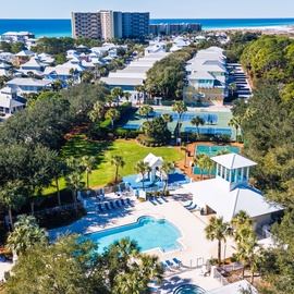 Aerial view of a resort community featuring pool facilities, recreational areas, and nearby beach access in a lush coastal setting.