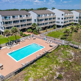 Aerial view of multi-story beachside resort buildings with swimming pool and deck area surrounded by natural coastal vegetation.