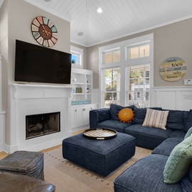 Sink into plush navy sectionals by your cozy fireplace, where vaulted ceilings and coastal charm create the perfect gathering spot for evening relaxation.