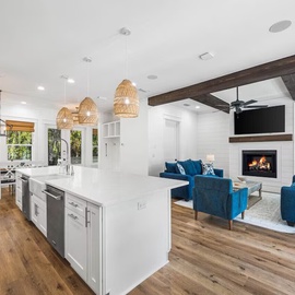 Unwind in your open-concept haven where modern kitchen flows into cozy living space with fireplace warmth and vibrant blue seating.
