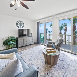 Relax in your bright living room with stunning ocean views through floor-to-ceiling windows and tropical palm trees swaying outside.