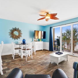 Relax in your bright coastal living space with ocean-themed decor, tropical ceiling fan, and private balcony overlooking swaying palms.