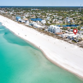 Aerial view of pristine white sand beach with crystal-clear turquoise waters and beachfront vacation homes.