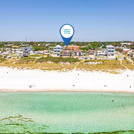 Aerial view of a pristine beachfront community nestled along crystal-clear turquoise waters, bordered by sandy shores and coastal homes.